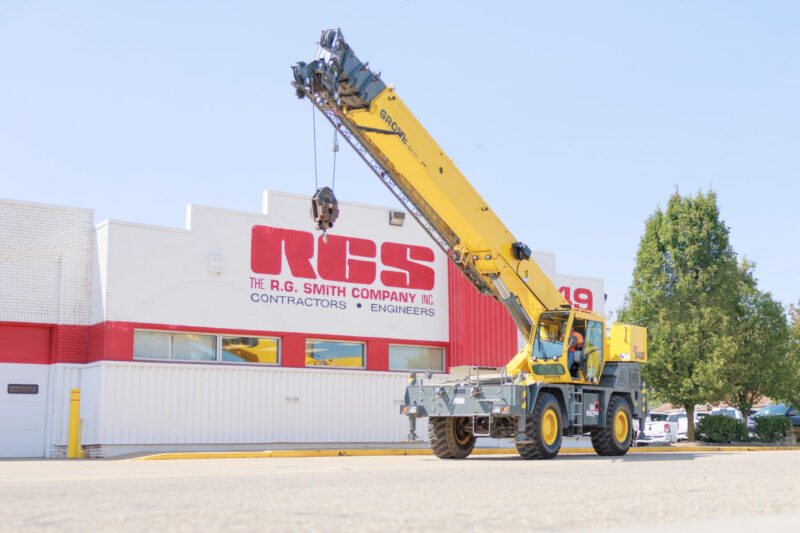 A yellow crane is operating in front of a building with "R.G. Smith Company, Inc." signage on a clear day.